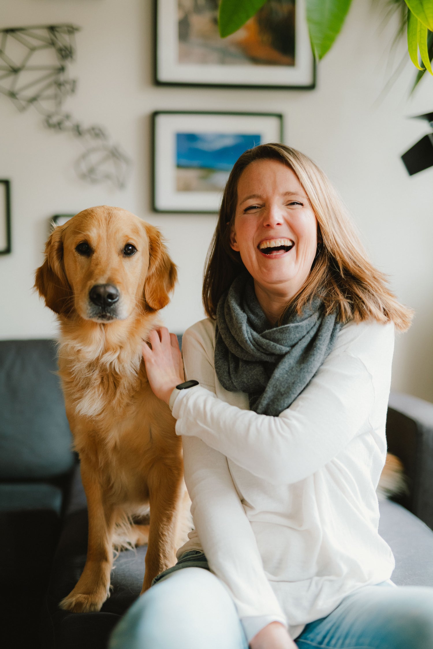 Eine Frau und ein Hund sitzen auf einem Sofa. Die Frau lacht in die Kamera